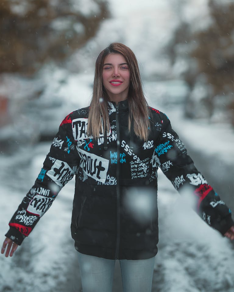 Smiling woman enjoying snowfall, showcasing winter fashion with a patterned jacket.